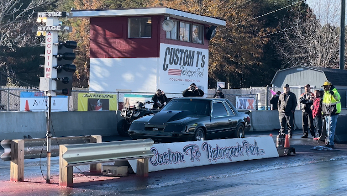 A view of a motorsport drag strip with cars getting ready to race on the track with workers waiting on the side.