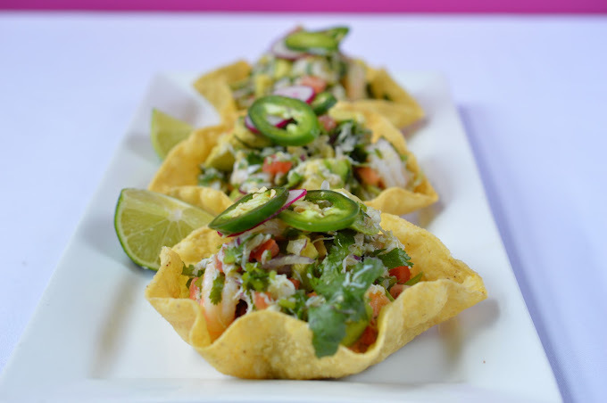 A view of an chip filled with an mixture of vegetables, topped with jalapenos and a sides of sliced lime.