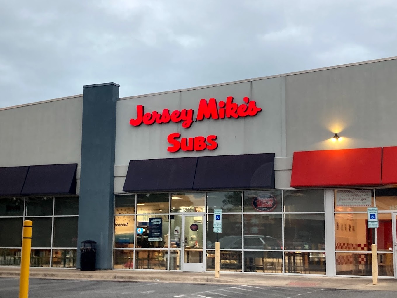 An outside view of an sandwhich shop, with red awnings covering the door and windows, and red lettering above the doors and windows reading "Jersey Mike's Subs"