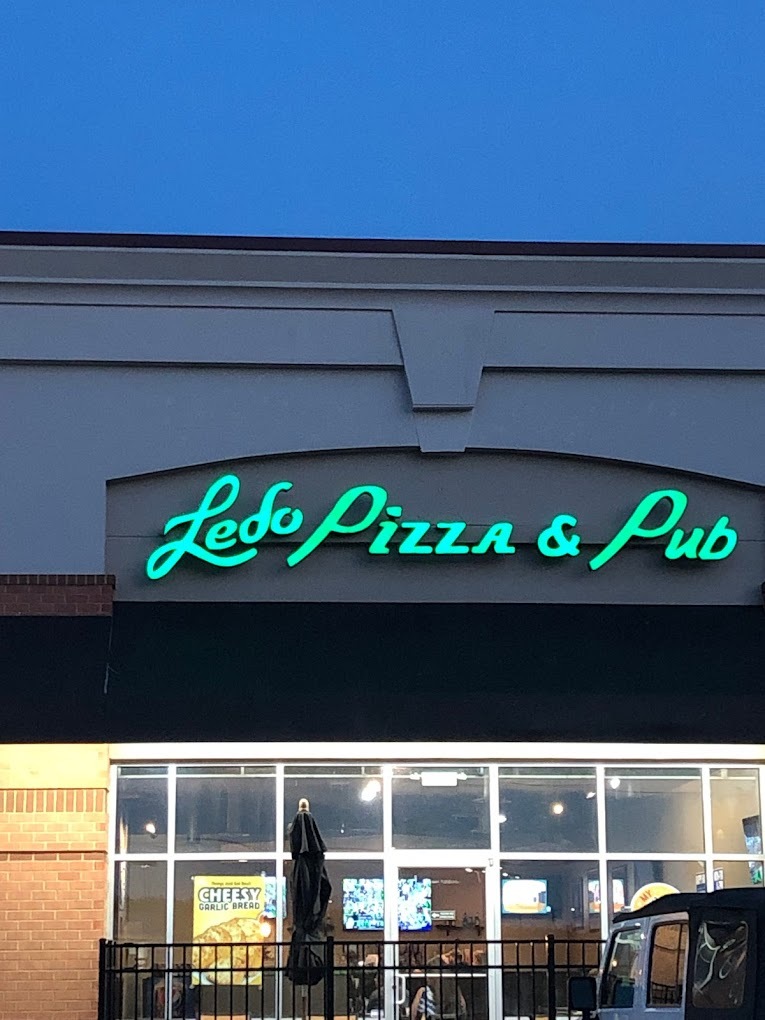 An outside view of a pizzeria with green lettering reading "Ledo Pizza & Pub" above the awning above the door and windows.