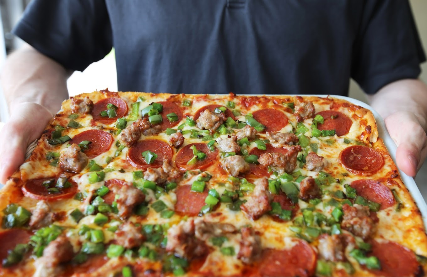 A view of a large rectangular pizza topped with cheese, pepperoni, sausage, and chives.