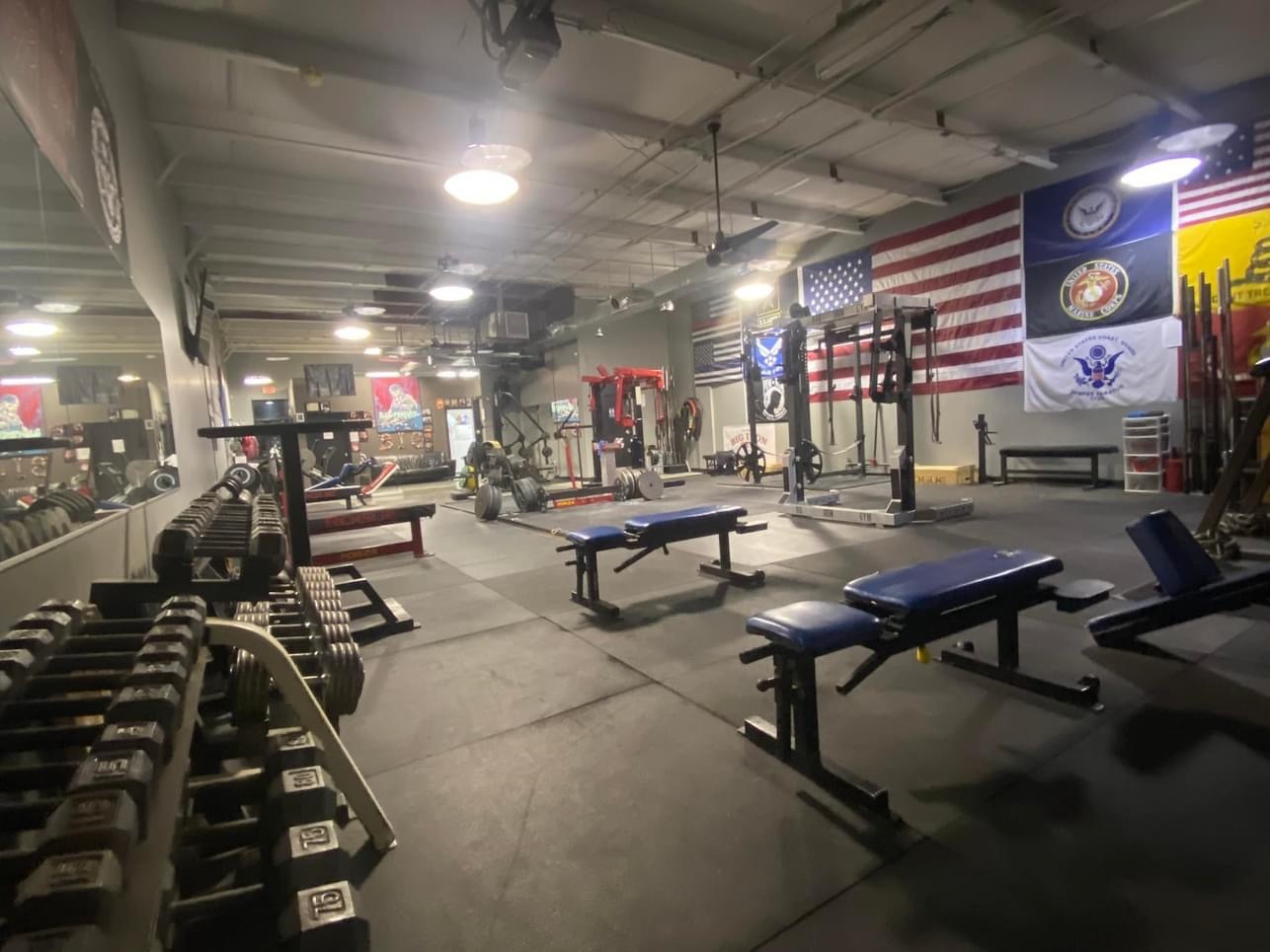 An inside view of a gym with various flags lining the wall, the room is filled with lots of different work out equipment.