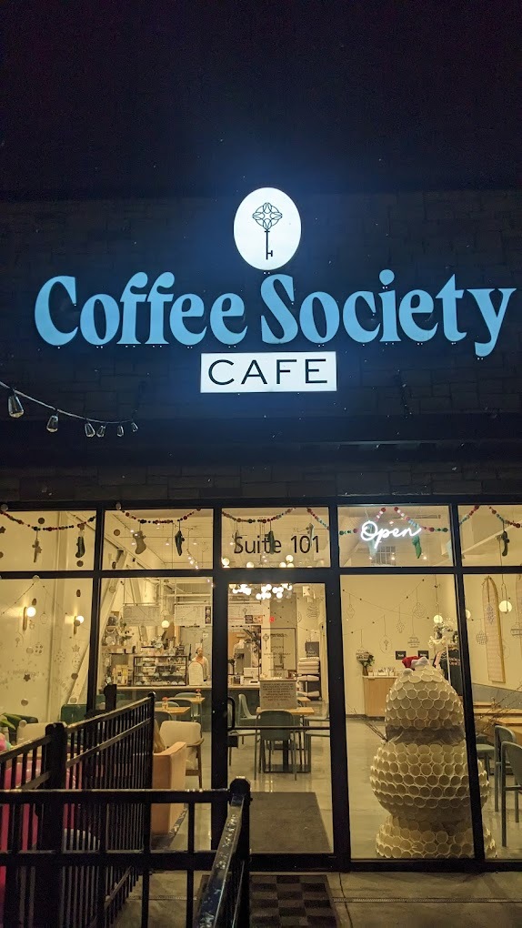 An outside view of a coffee shop at night with blue lettering at the top of the glass door.