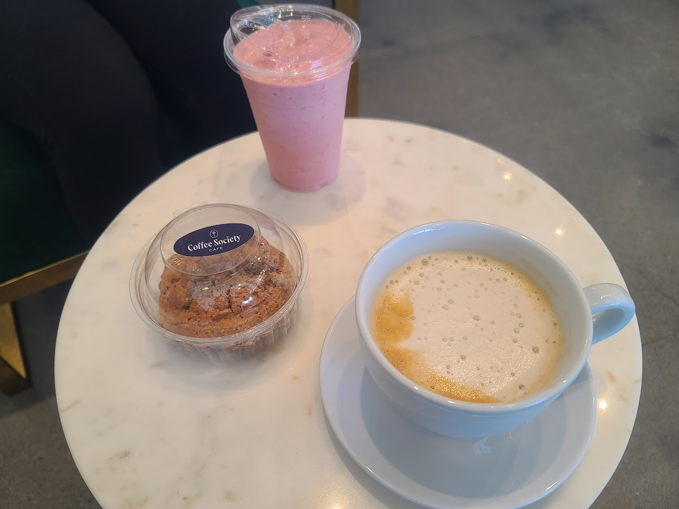 A white table with a latte, pink smoothie, and muffin a top the table.