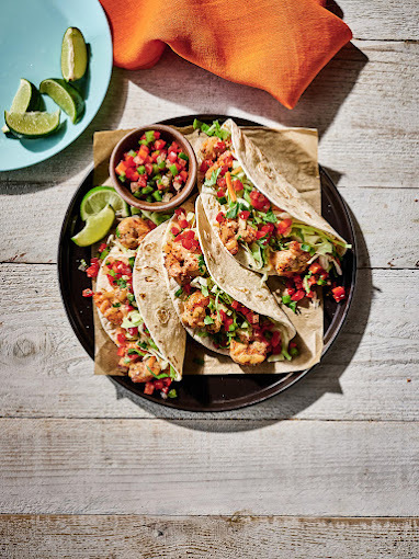 A black serving plate consisting of tacos loaded with protein and veggies and a side of Pico de Gallo.
