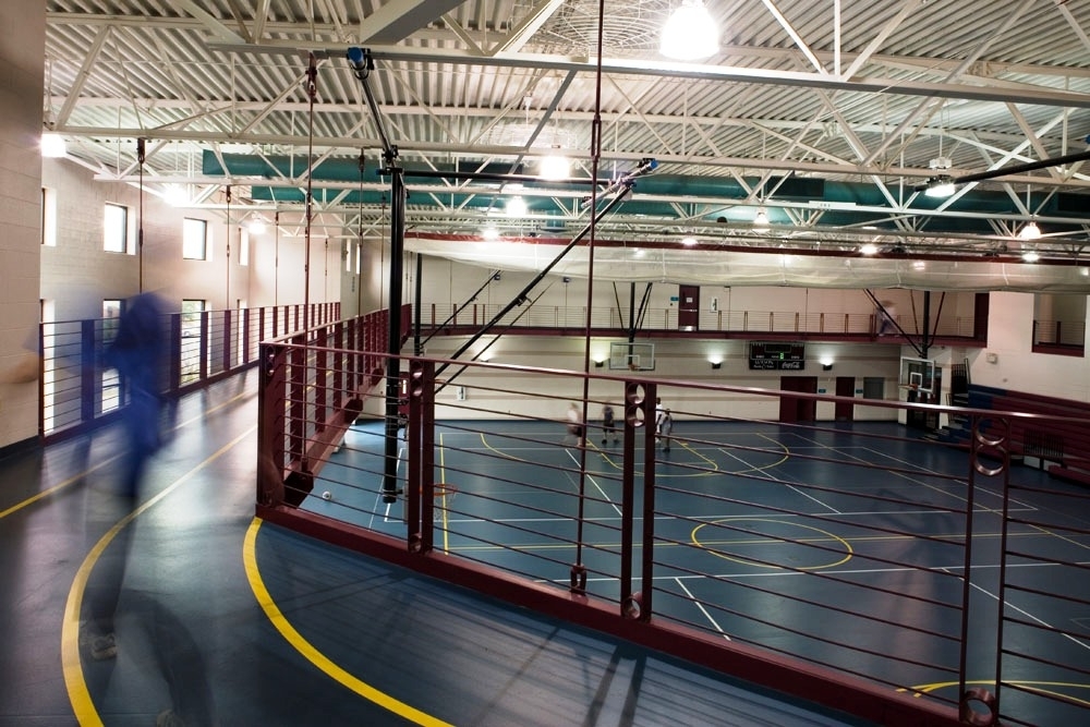 An view of a court and an raised running track inside a very large gym building that is above the gym floor below.