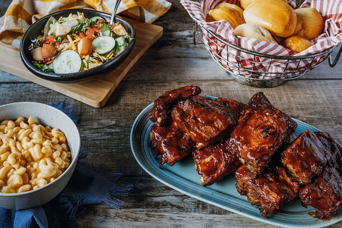 An view of a spread of various dishes including chicken wings, mac and cheese, a salad, and a basket full of bread rolls.