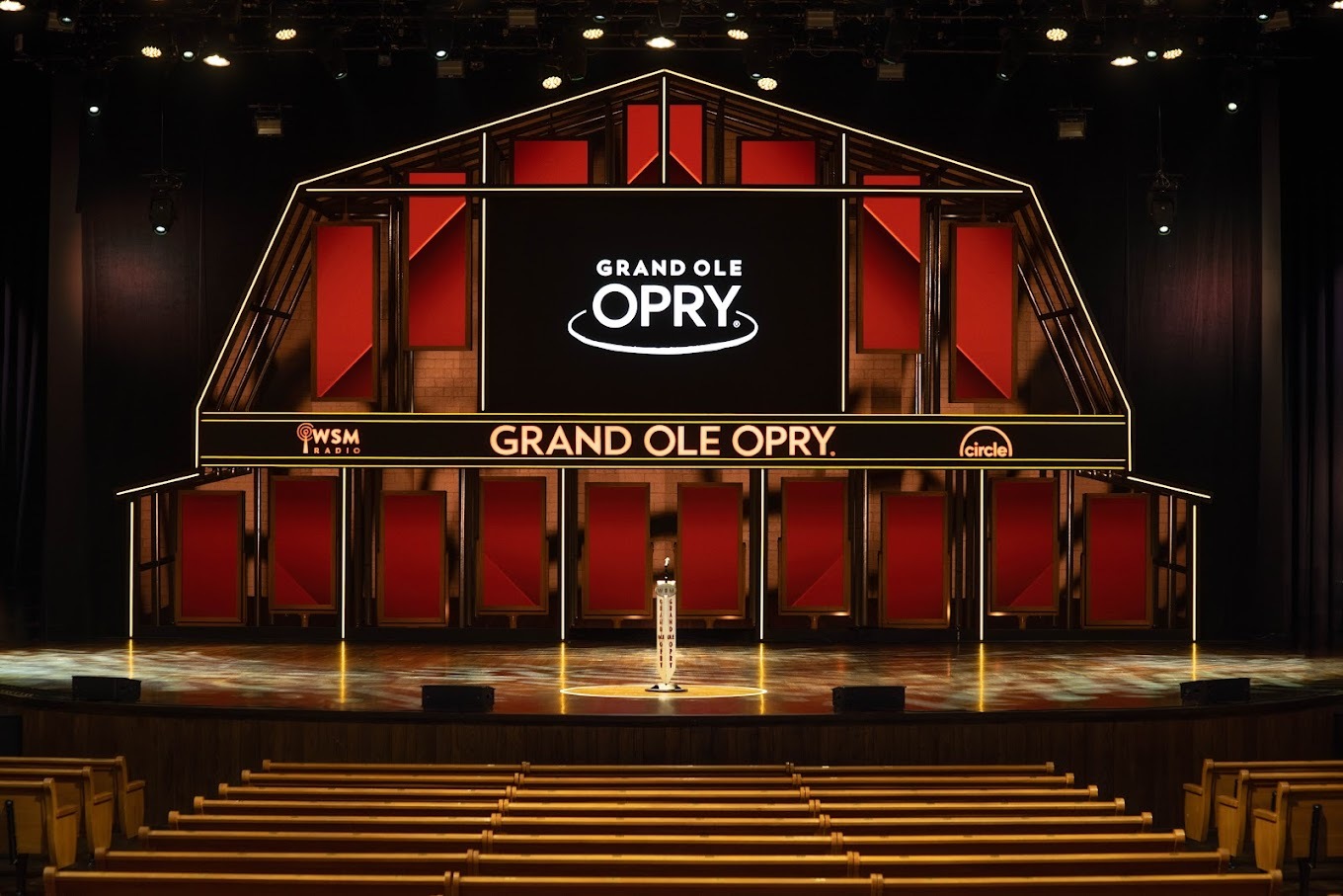 An inside view of a music venue with a stage and a screen that resembles the shape of a barn.