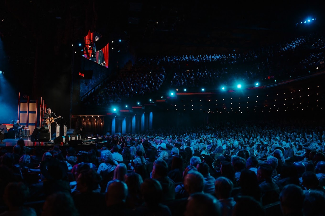 An view of a concert venue, full of participates and low blue lights cast a light blue light on the crowd.