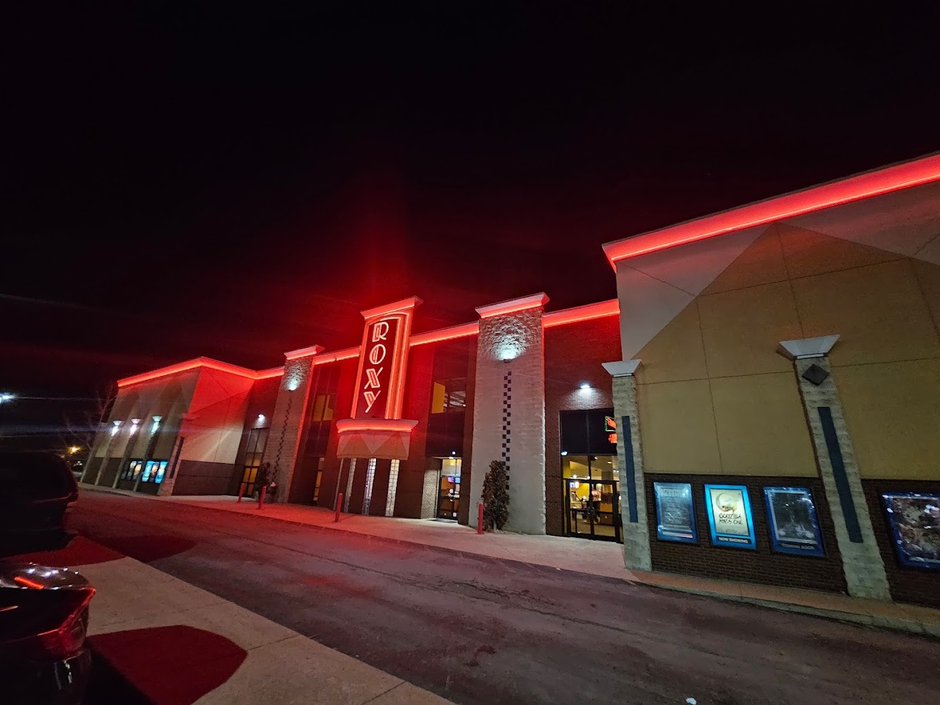 An outside view of an theatre with red neon lights lining the top of the building and the sign above the door.