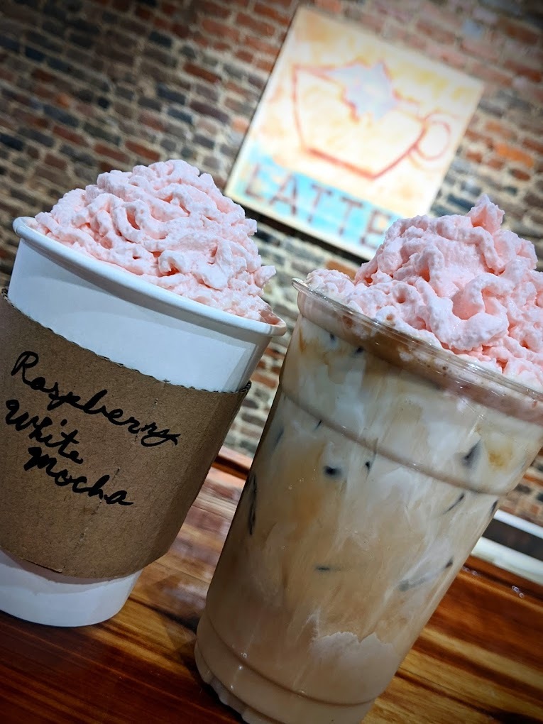 an view of two coffees sitting next to each other topped with strawberry whipped cream.