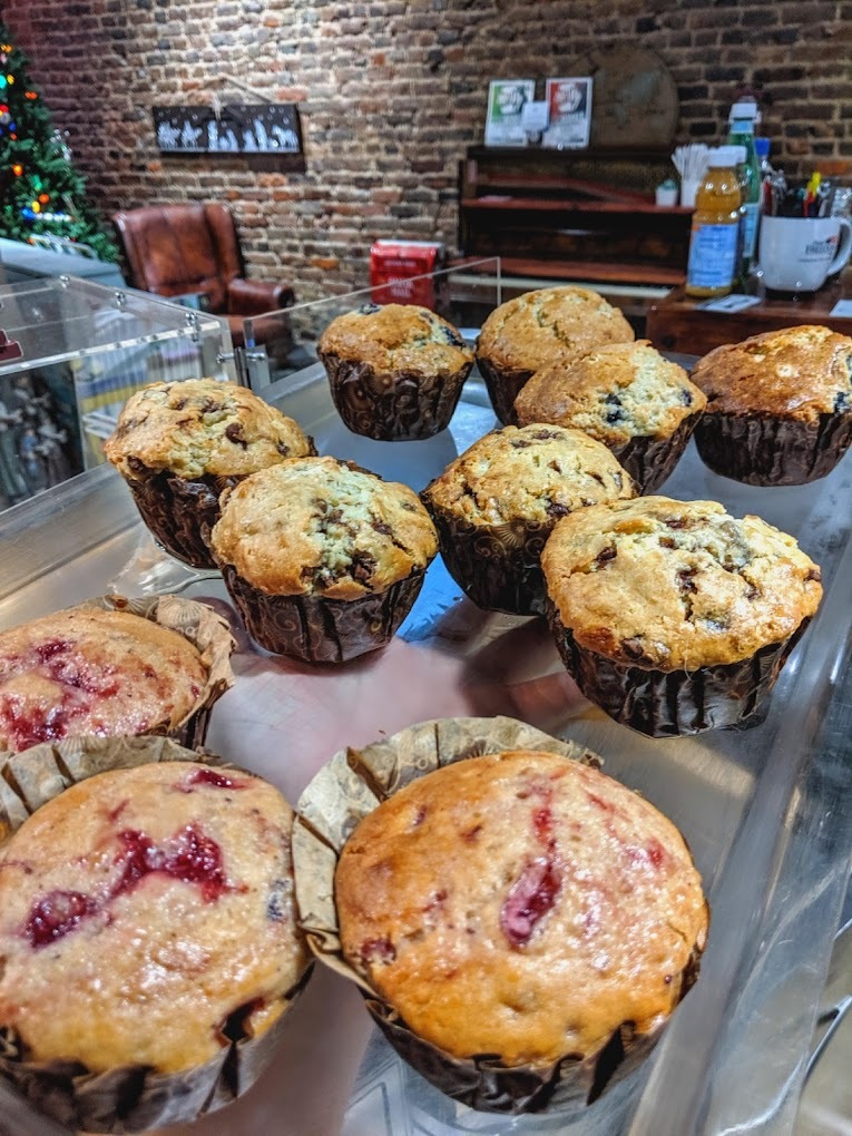 An close up view of a bakery tray with various kinds of muffins such as raspberry and chocolate