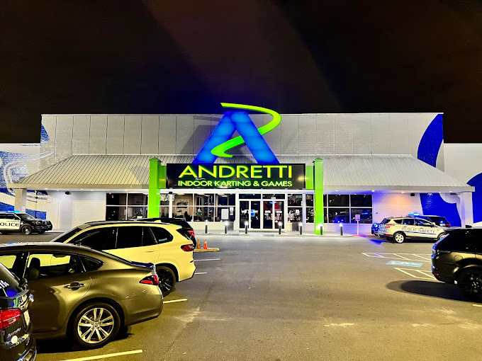 Exterior night view of a beige building with green and blue neon signs above the door that read "Andretti Indoor Karting and Games."