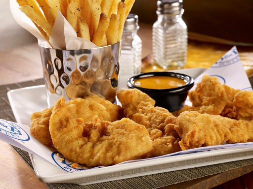 Fries in a metal cup, breaded chicken, and an orange sauce all on a white plate. There are salt and pepper shakers in the background.