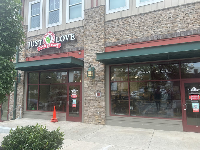 Downtown vibe of a light brown and rock accented building. It has a green sunshade and red accents. The sign above the door reads "Just Love," with their green and red logo in between the words.