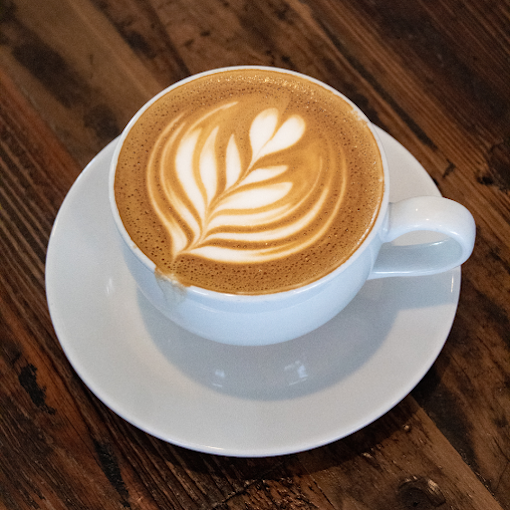 Heart shaped foam art latte in a white cup on a white saucer.