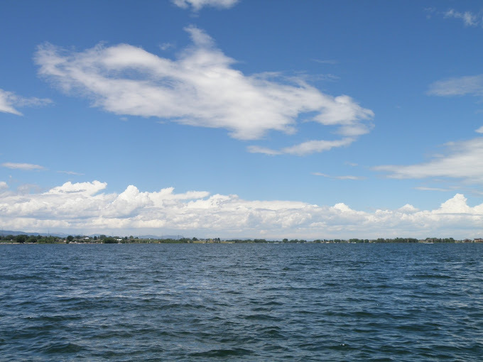 Lake with some visible land on the horizon line, and a mildly cloudy sky.