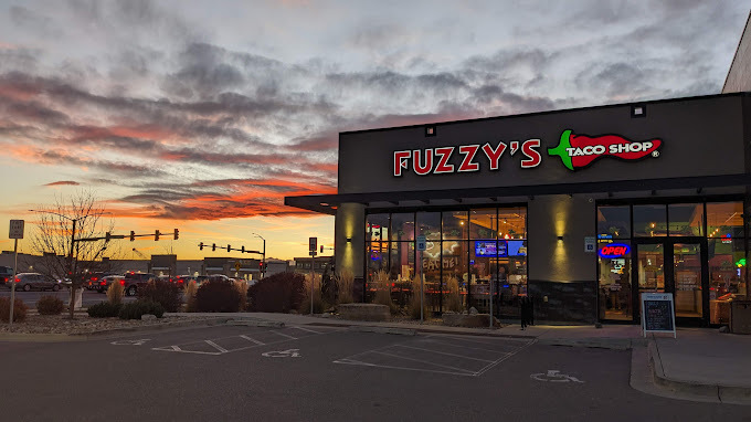 Exterior view of a building with glass windows and bracketed sunshades. The sky in the background is a sunset.