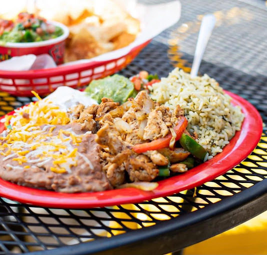 Rice, chicken, and cheese in a red plate that is resting on a black wire-like table.