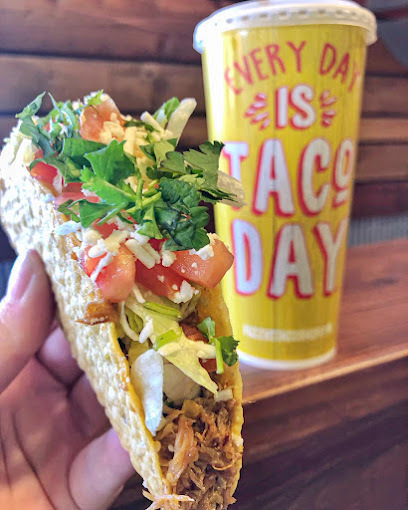 Hand holding a taco with tomatoes, meat, and greens. A yellow cup in the background states "Every day is taco day."
