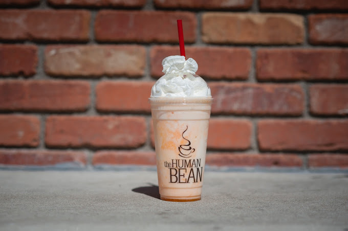 Light orange colored drink with whipped cream and red straw in front of a brick wall.