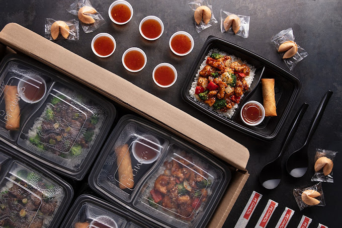 High view of a take-out packaging process spread of Asian food. Four boxes are already packed, with sauces and fortune cookies ready to be added to additional containers.