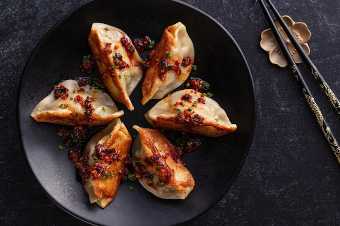 Dumplings aligned in a swirl pattern on a black plate, with chopsticks set on the side.