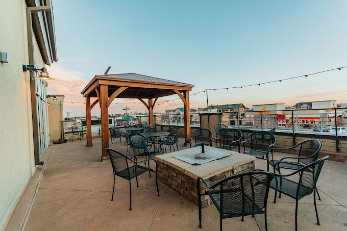 View of roof patio with fire pit and wooden sun canopy. Chairs and tables are black wire lattice.