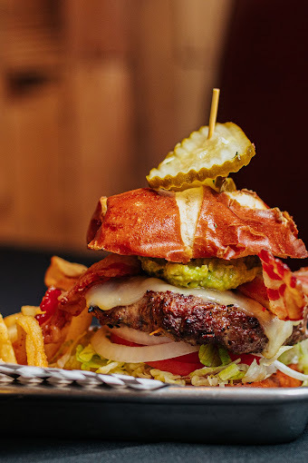 Burger with bacon, onion, tomatoes, and lettuce. A toothpick and pickle are stuck through the top bun.
