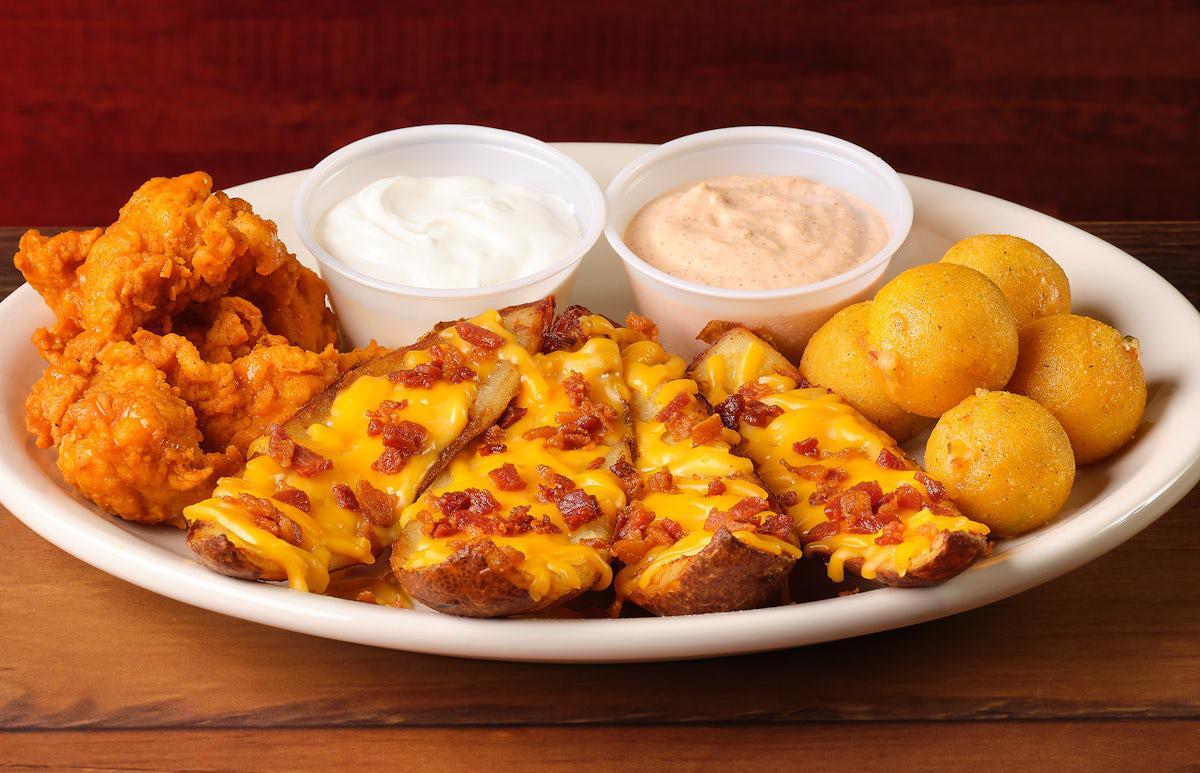 White plate with different appetizers, chicken, loaded potato skins, and hush puppies. Served with two containers of sauce.