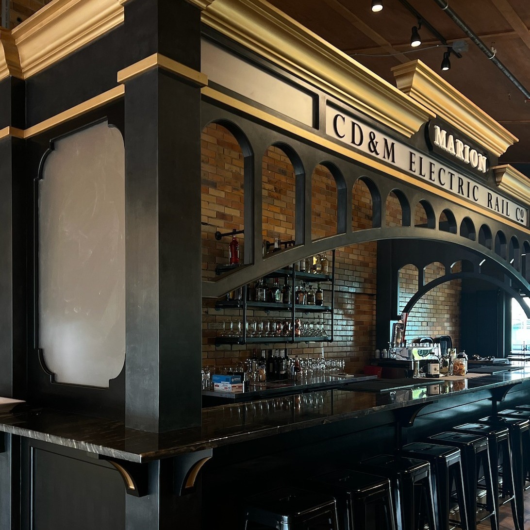Bar counter with a brick wall and railway-themed table pieces. The sign on the top says "Marion CD&M Electric Rail Co."