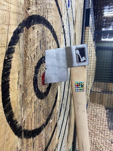 Close view of an axe centered in the bullseye of a wooden target.