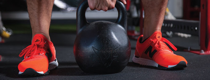 Man about to lift a large dumbbell. His shoes are bright orange New Balances.