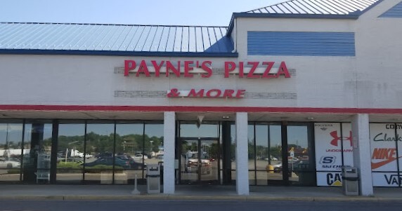 Beige building with blue roofing. There are a lot of glass windows and doors, as well as three square columns in front of the entrance. The red sign above the door entrance says "Payne's Pizza and more."