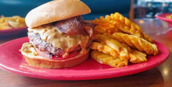 Burger with patty, cheese, tomato, and bacon, as well as waffle fries, all on a red plate.