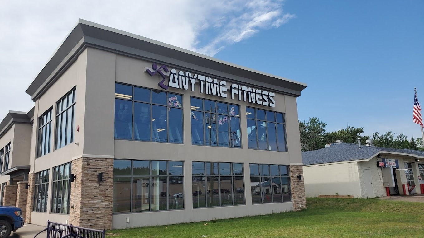 A view of a gray and tan brick building with large windows and white lettering reading "Anytime Fitness"