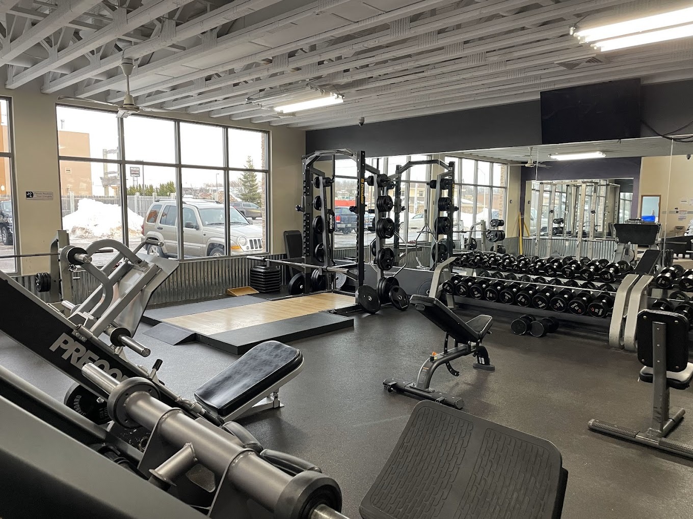 A view of a room with large windows and filled with all different kinds of workout equipment.