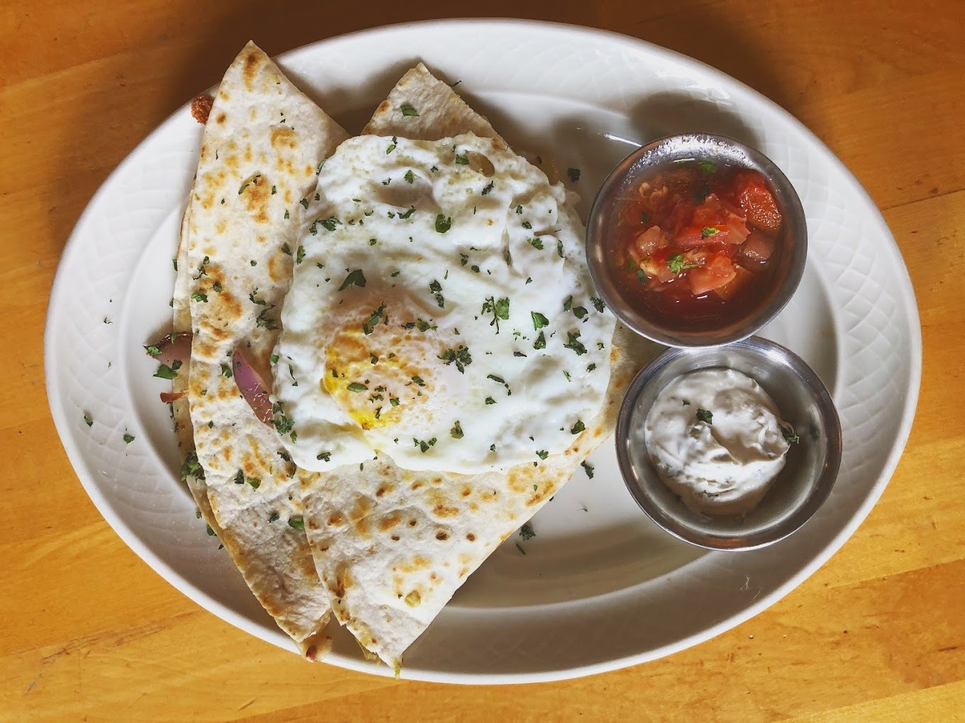 A white plate with a view of a sunny side up egg with two tortillas, and two sides of different kinds of sauces.