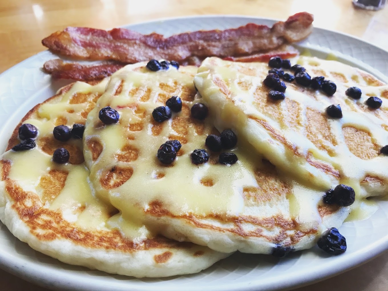 A view of three pancakes on a white plate with a side of bacon.