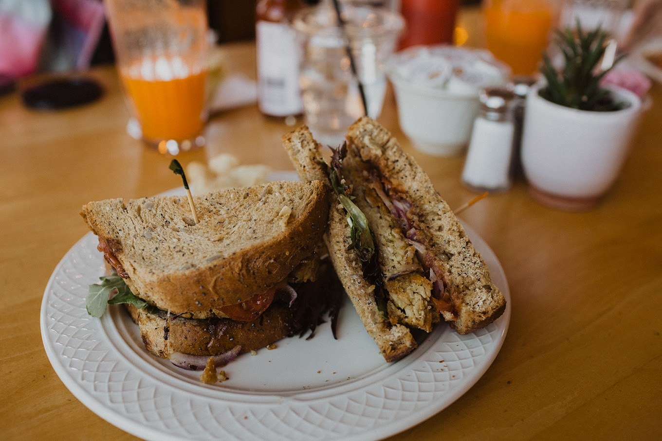 A view of a sandwich on a white plate the sandwich consisting of chicken, onion, lettuce and sauce.