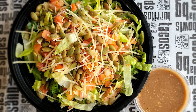 A view of a black plate consisting of a salad topped with tomatoes, guacamole, and cheese.