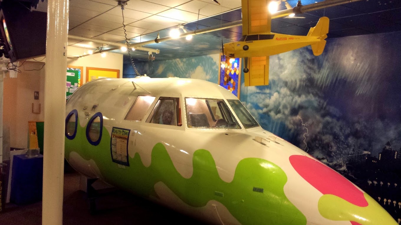 A view of a room with a model plane inside, painted white with colorful wavy green designs and pink circles