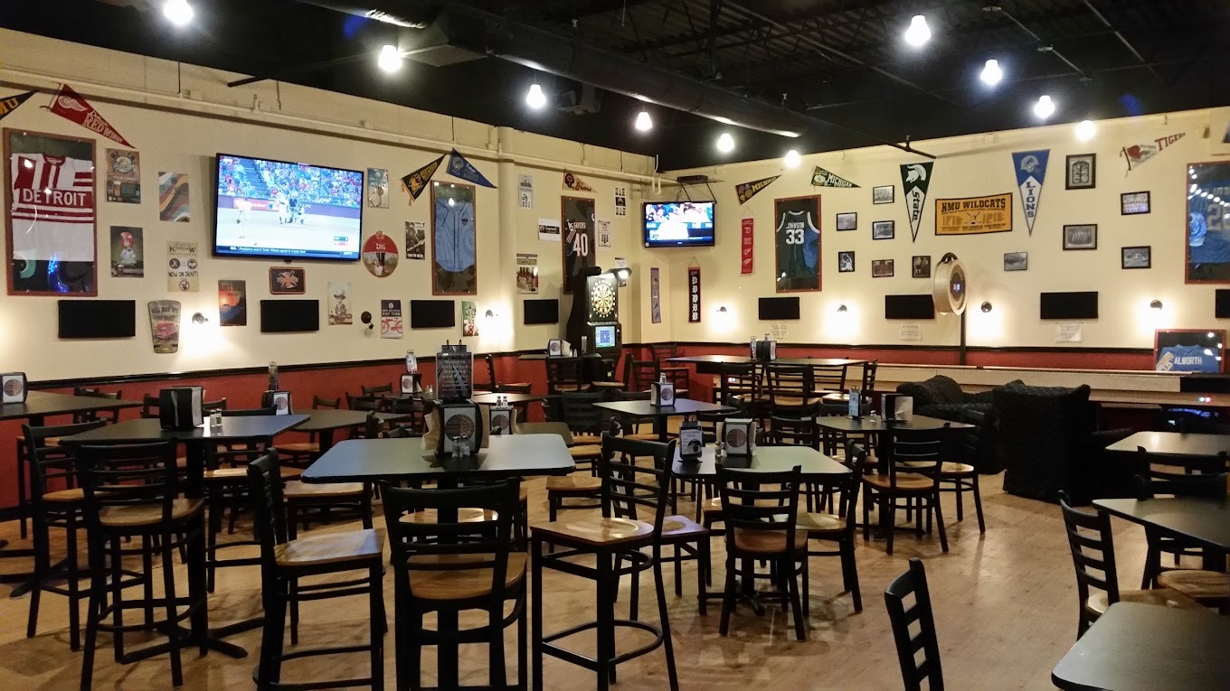 A view of a dining area that is dimly lit, the walls are covered with decoration and loads of tables and chairs are in the middle and along the walls.