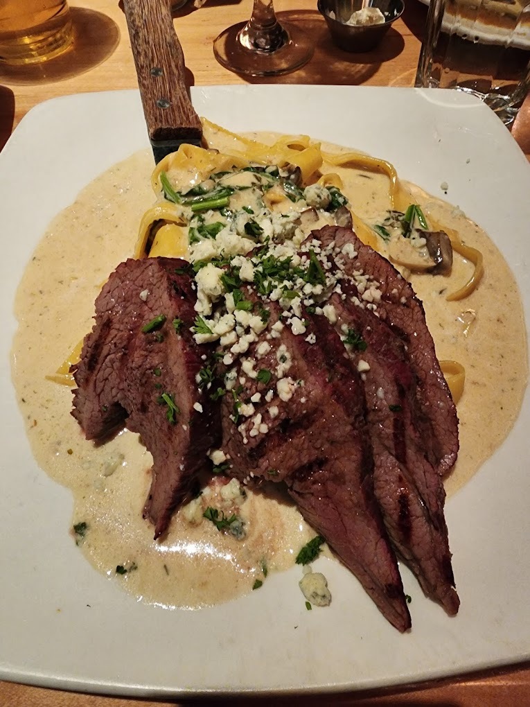 Plate of fettuccine noodles and alfredo sauce with steak, topped with feta cheese and green garnish.