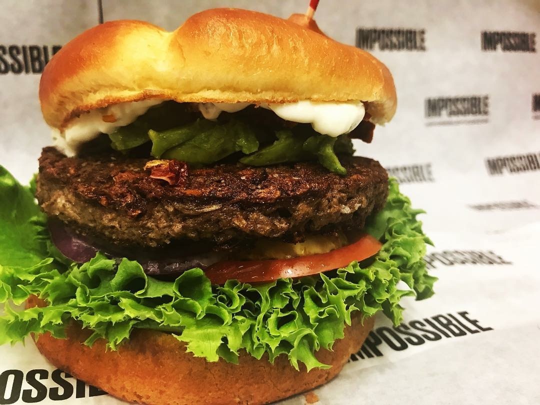 Photo of a burger slightly opened to see the ingredients of lettuce, patty, and tomato.