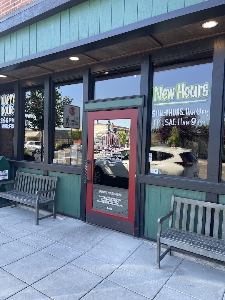 Front entrance to a bar with green siding, and a red door with two benches to the left and the right of the door.