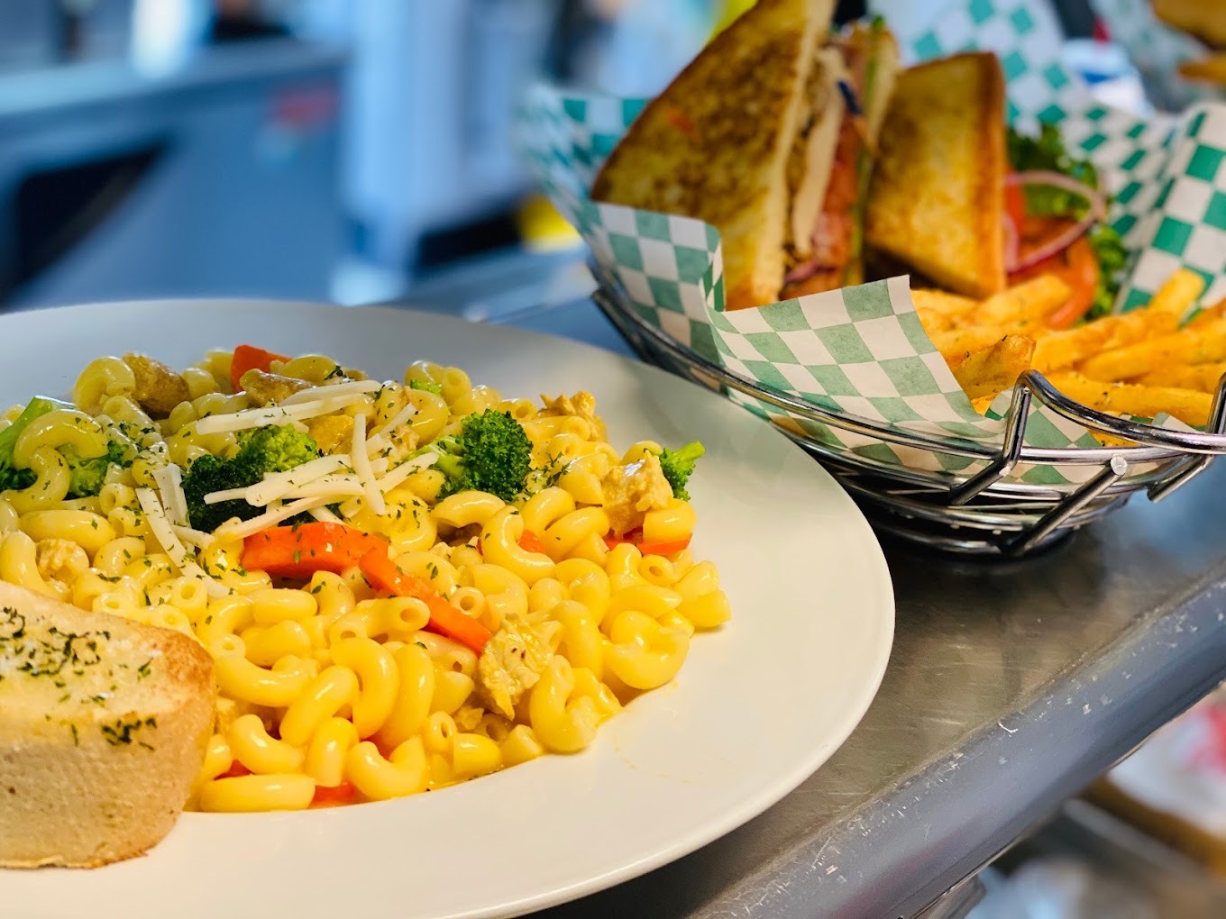 Photo of a loaded veggie macaroni on a plate and a basket with a home-style sandwich and fries.