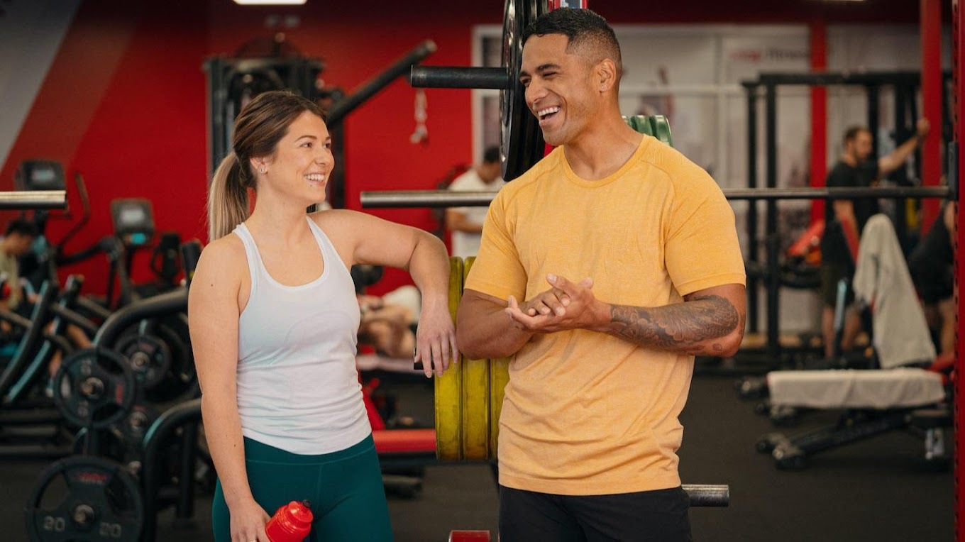 An view of two people chatting up against workout equipment, in a gym environment.
