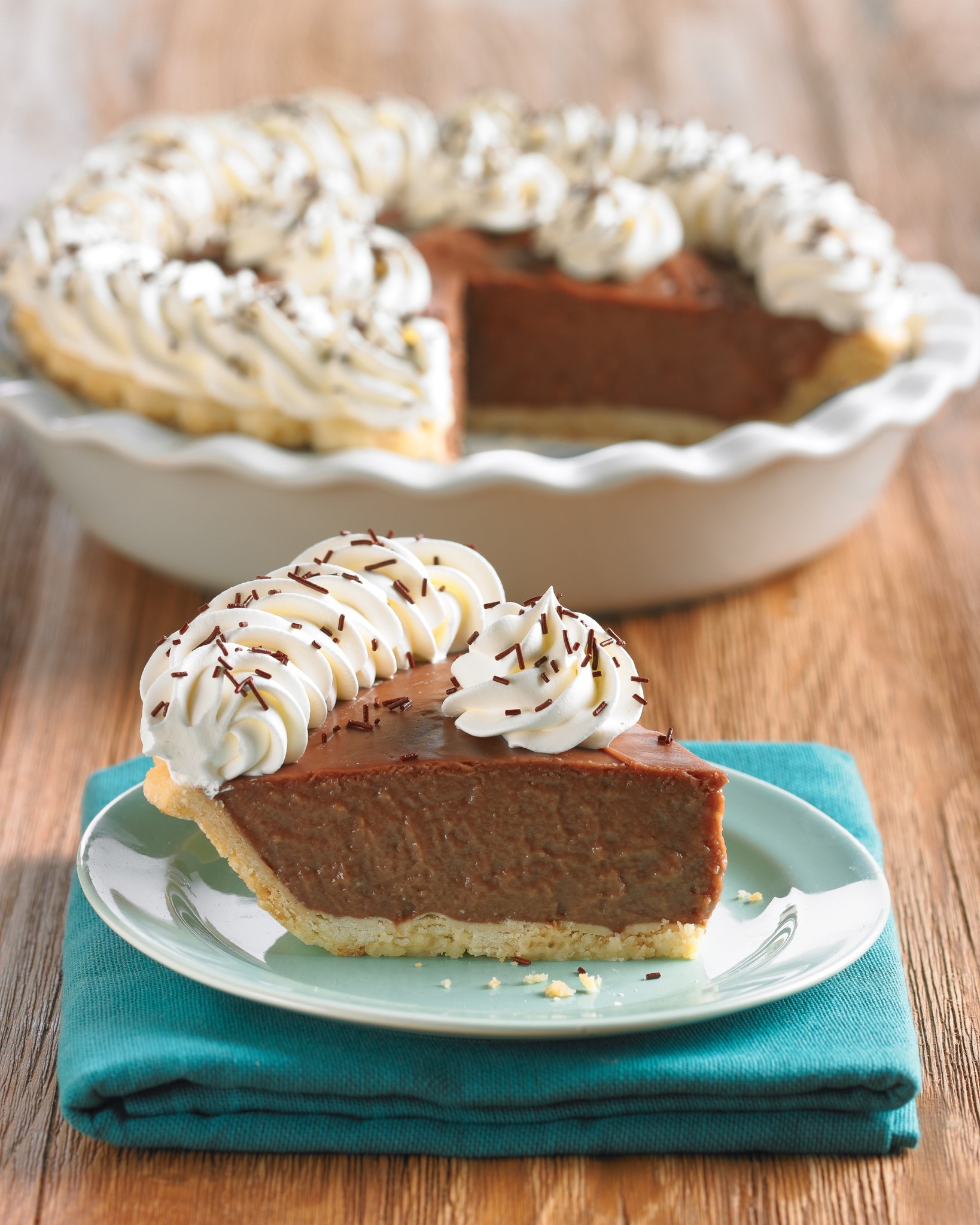Chocolate pie with white frosting and brown sprinkles. One slice is taken out of the pie and placed on a teal napkin.