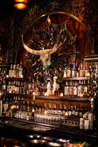 Wall of alcoholic beverages. An animal with long horns and colored marking is hung in the middle of the wall.